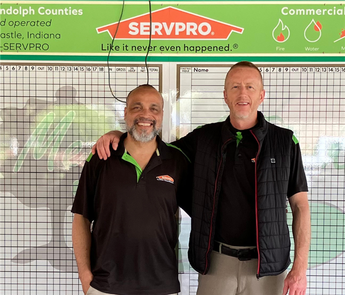 Two SERVPRO employees smiling near a golf score board